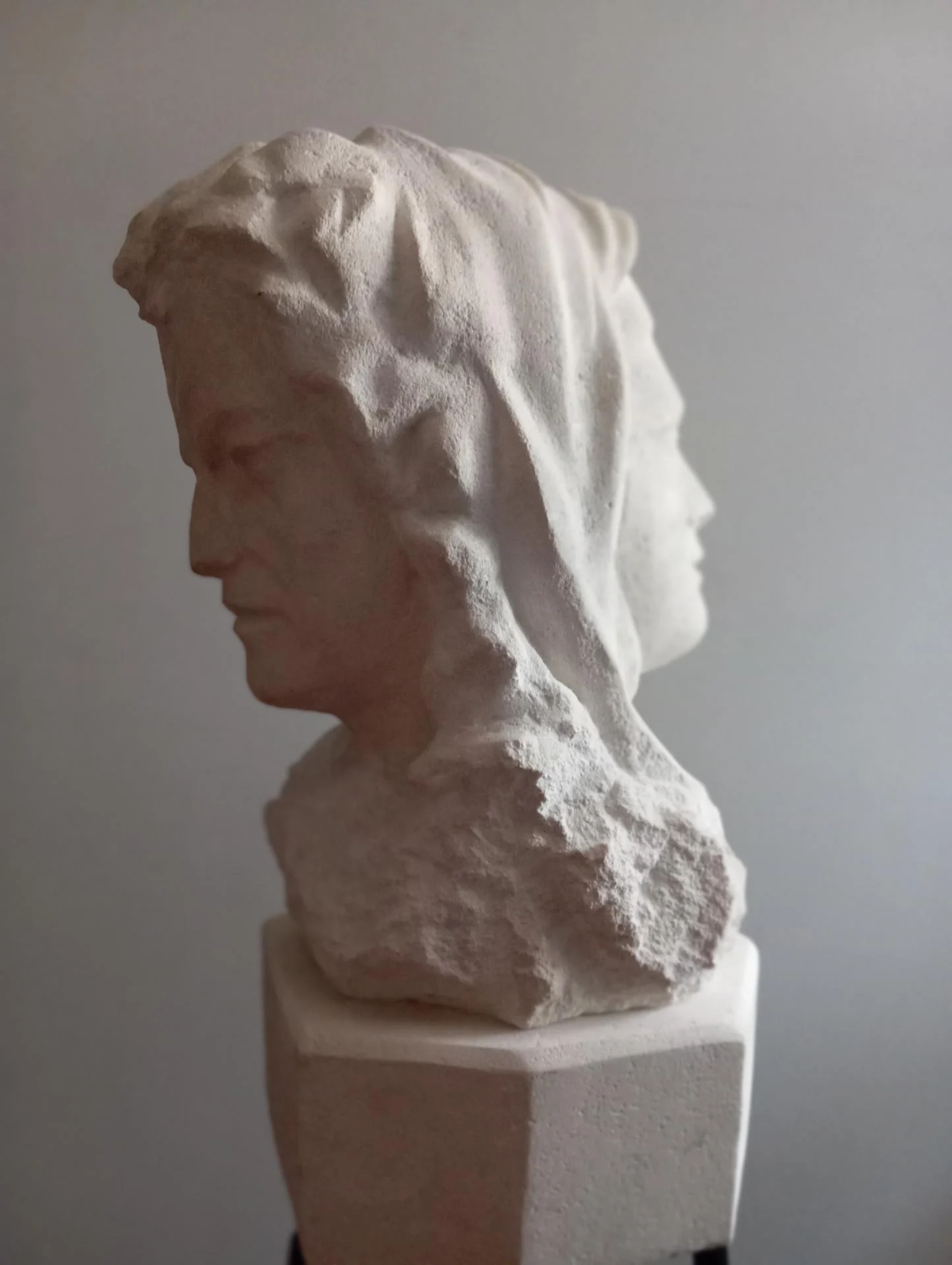 Buste bicéphale en pierre calcaire naturelle, les deux profils dos à dos — le révolutionnaire au premier plan, visage baissé vers la terre, et la carmélite de Compiègne voilée derrière, visage levé vers le ciel : le bourreau et la martyre taillés dans le même bloc. Taille directe à la main, hauteur 60 cm dont socle 10 cm, 2025. Une réflexion sculptée sur le sens de la vie : qu'est-ce que Vivre ? Pièce unique signée, disponible, 4 500 €. Sculpteur d'art sacré Jean-Joseph Chevalier, atelier de Brignoles (Var, Provence).