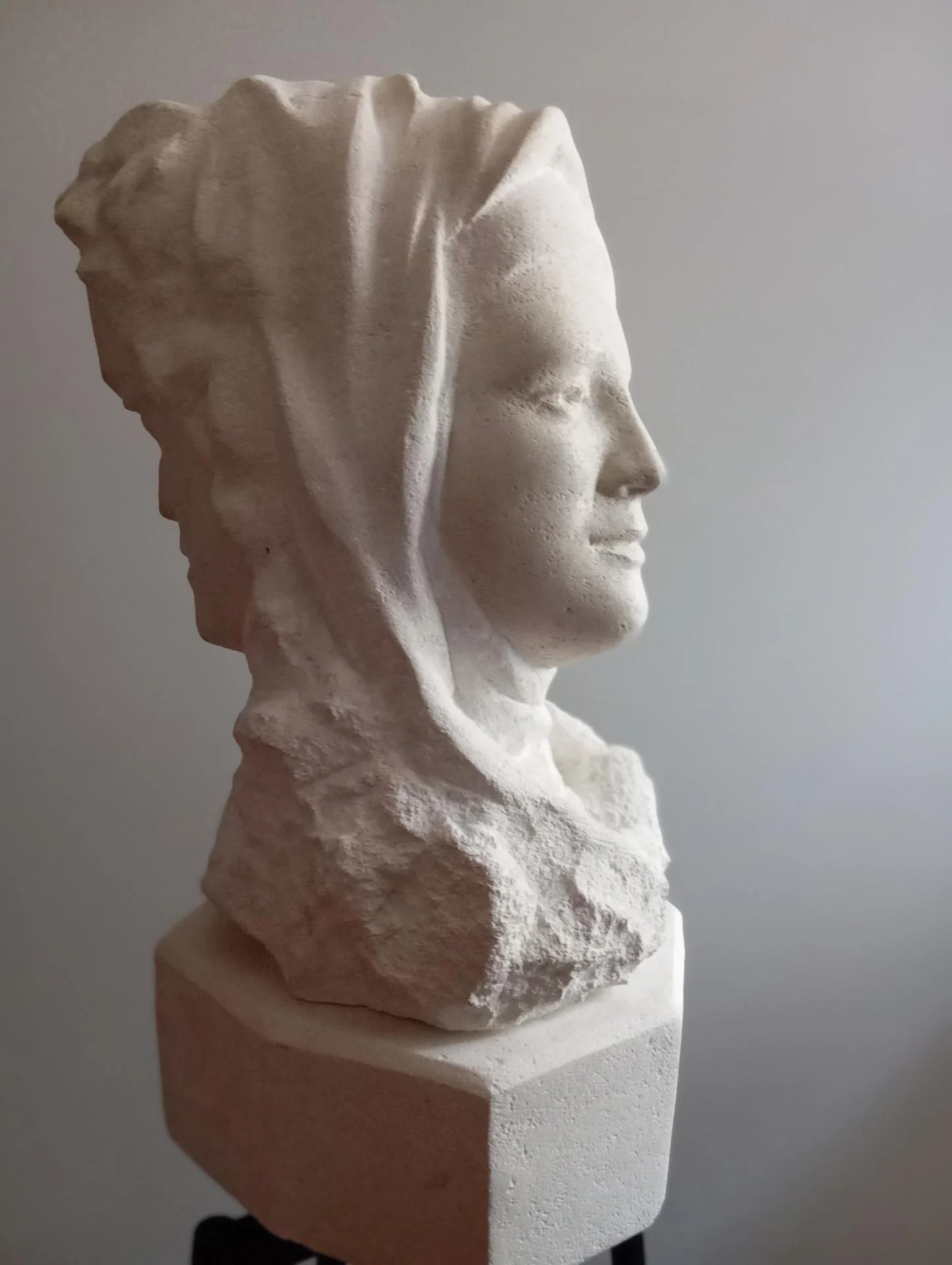 Le profil de la carmélite — le visage levé vers le ciel, serein, sous le voile de pierre ; derrière elle, la masse brute du bloc. Buste bicéphale en pierre calcaire naturelle, taille directe, 60 cm, 2025. Sculpteur d'art sacré Jean-Joseph Chevalier (Brignoles, Var, Provence).
