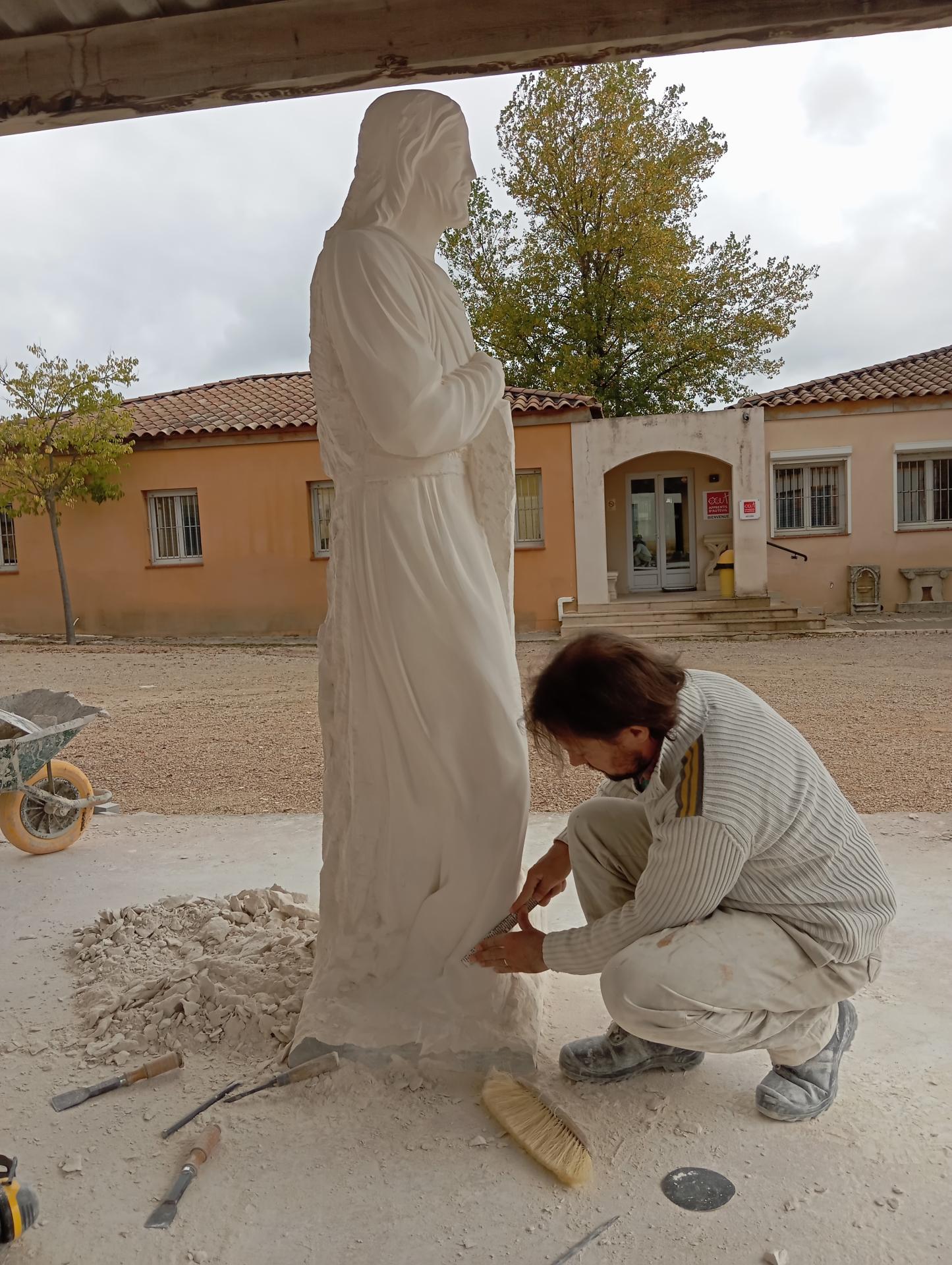Détail aux pieds du Christ charpentier — finitions des plis de la tunique et du socle, taille directe pierre calcaire — atelier Jean-Joseph Chevalier