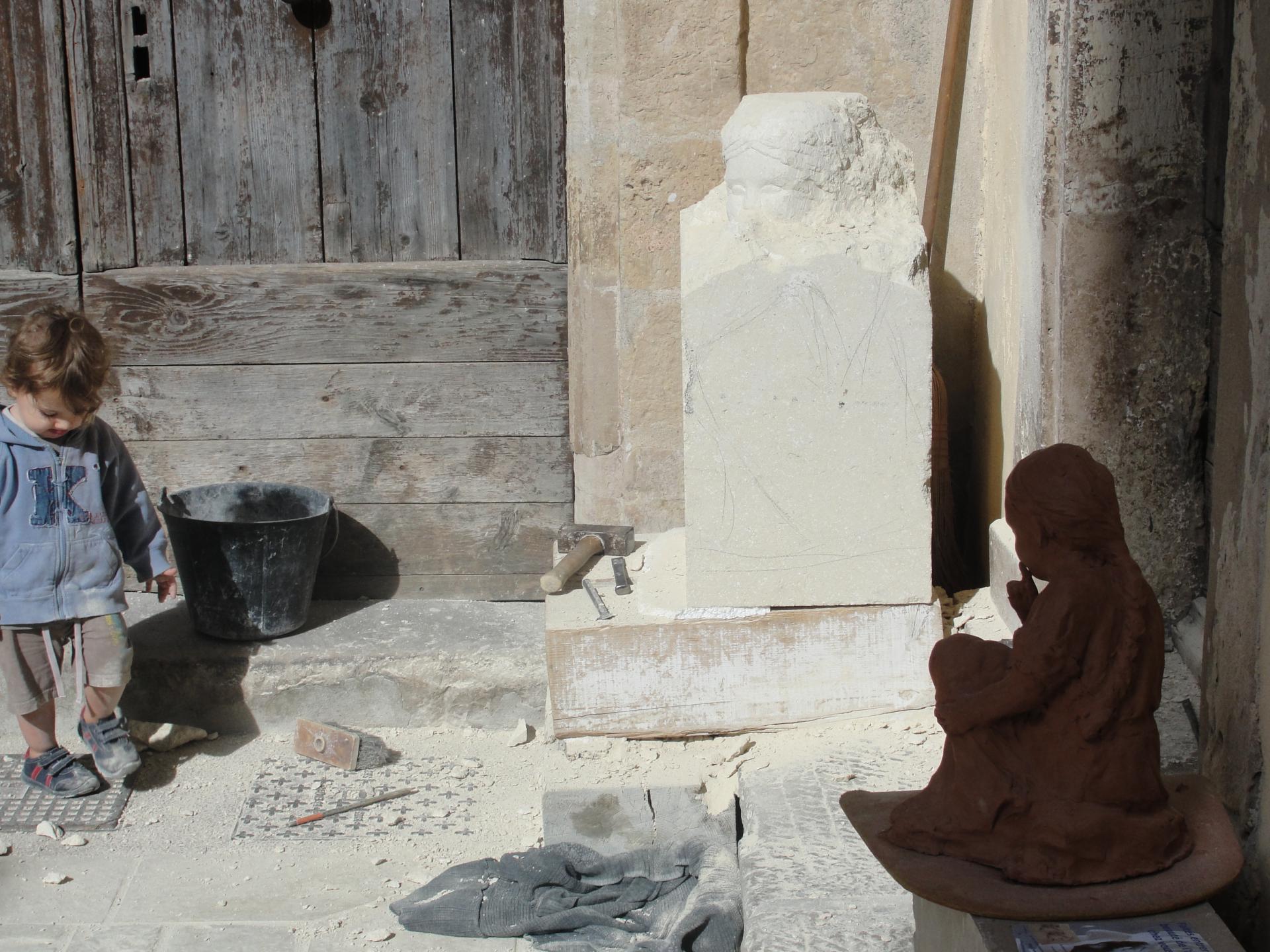 En atelier — prototype en terre de la Fillette au Silence, petit garçon debout donne l'échelle, pierre calcaire en taille directe en fond, Jean-Joseph Chevalier sculpteur