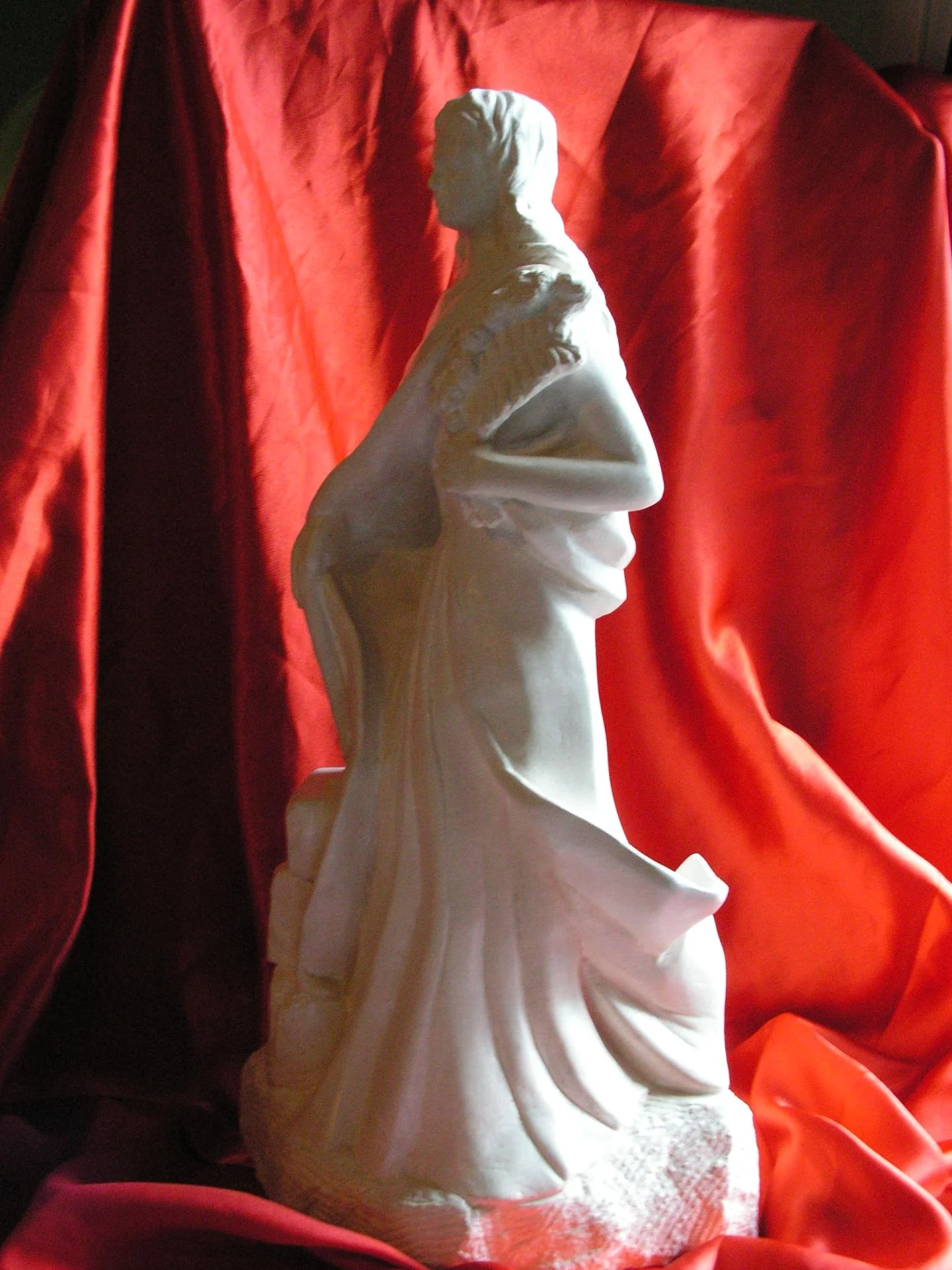 Statue Sainte Philomène vue de dos trois-quarts — les trois pierres gravées de l'épitaphe LUMENA PAX TE CUM FI visibles au sol depuis l'arrière, drapé en mouvement, ronde-bosse complète sans face privilégiée. Pierre calcaire naturelle blanche 70 cm, taille directe à la main par un sculpteur d'art sacré chrétien sur commande. Statue de dévotion privée pour oratoire de prêtre, presbytère, chapelle de séminaire — cadeau d'ordination sacerdotale 2008. Jean-Joseph Chevalier (atelier Brignoles Var, France).