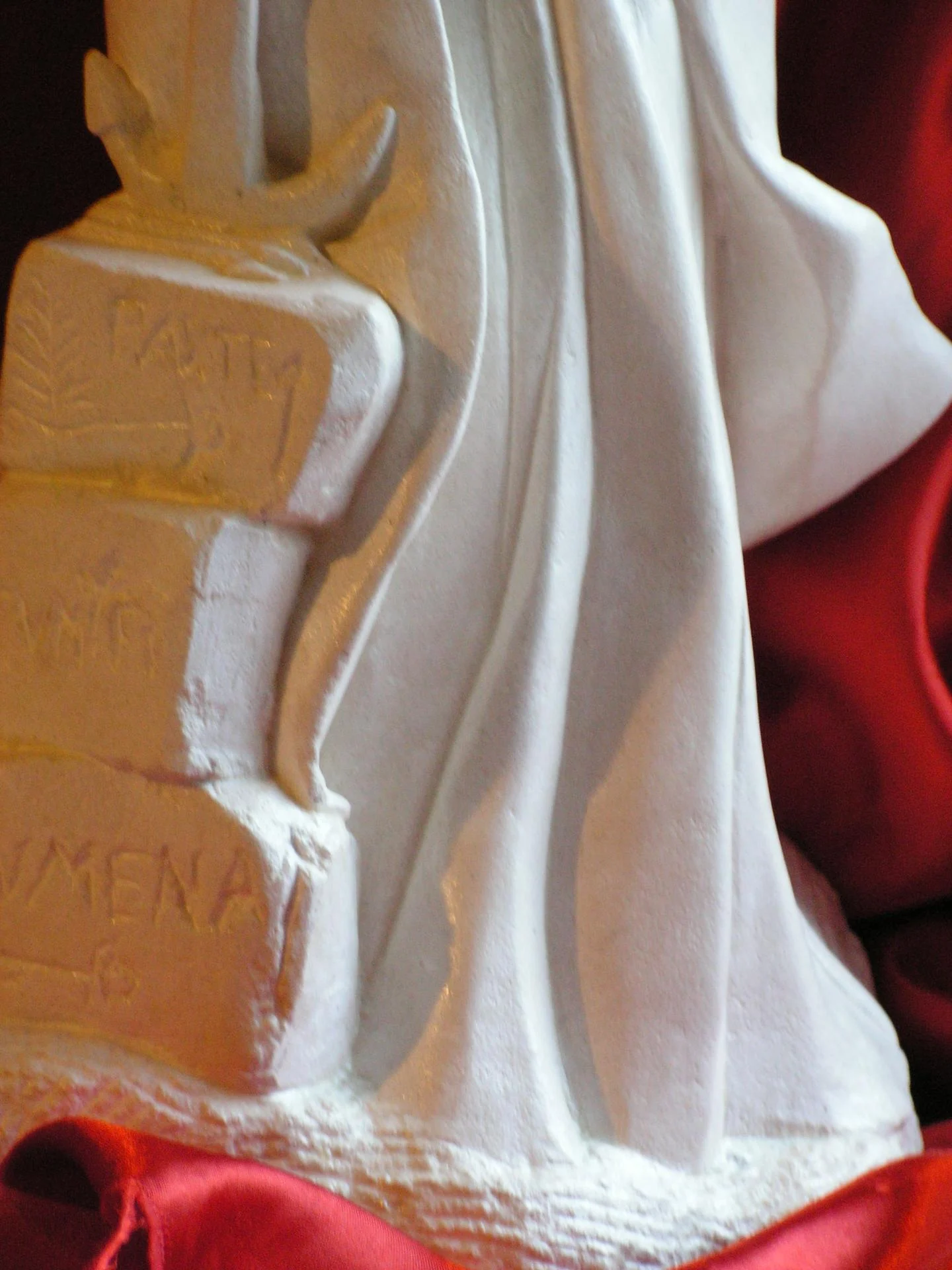 Détail du socle de la statue Sainte Philomène — trois pierres gravées en lettres capitales antiques de l'épitaphe LUMENA / PAX TE / CUM FI (Pax tecum Filumena, Paix avec toi Philomène), avec les flèches du martyre gravées. Transcription exacte de la dalle de la catacombe de Priscille à Rome découverte le 25 mai 1802. Archéologie sculptée en pierre calcaire naturelle blanche, taille directe à la main, sculpture religieuse pour cadeau d'ordination sacerdotale — Jean-Joseph Chevalier, sculpteur d'art sacré chrétien.