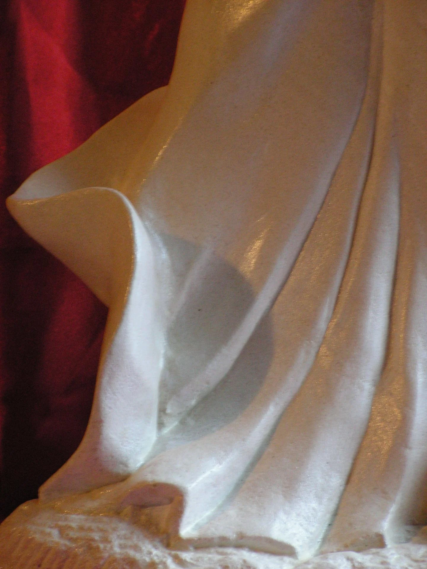 Détail du drapé de la statue Sainte Philomène — plis de la cape emportés par le vent du martyre, en mouvement, tournant autour du corps. Sculpture en pierre naturelle calcaire blanche 70 cm, taille directe à la main, signature de la statuaire chrétienne en ronde-bosse classique opposée à l'imagerie sulpicienne industrielle. Statue religieuse à faire faire chez un sculpteur sur pierre d'art sacré chrétien sur commande — cadeau d'ordination sacerdotale, atelier Jean-Joseph Chevalier.