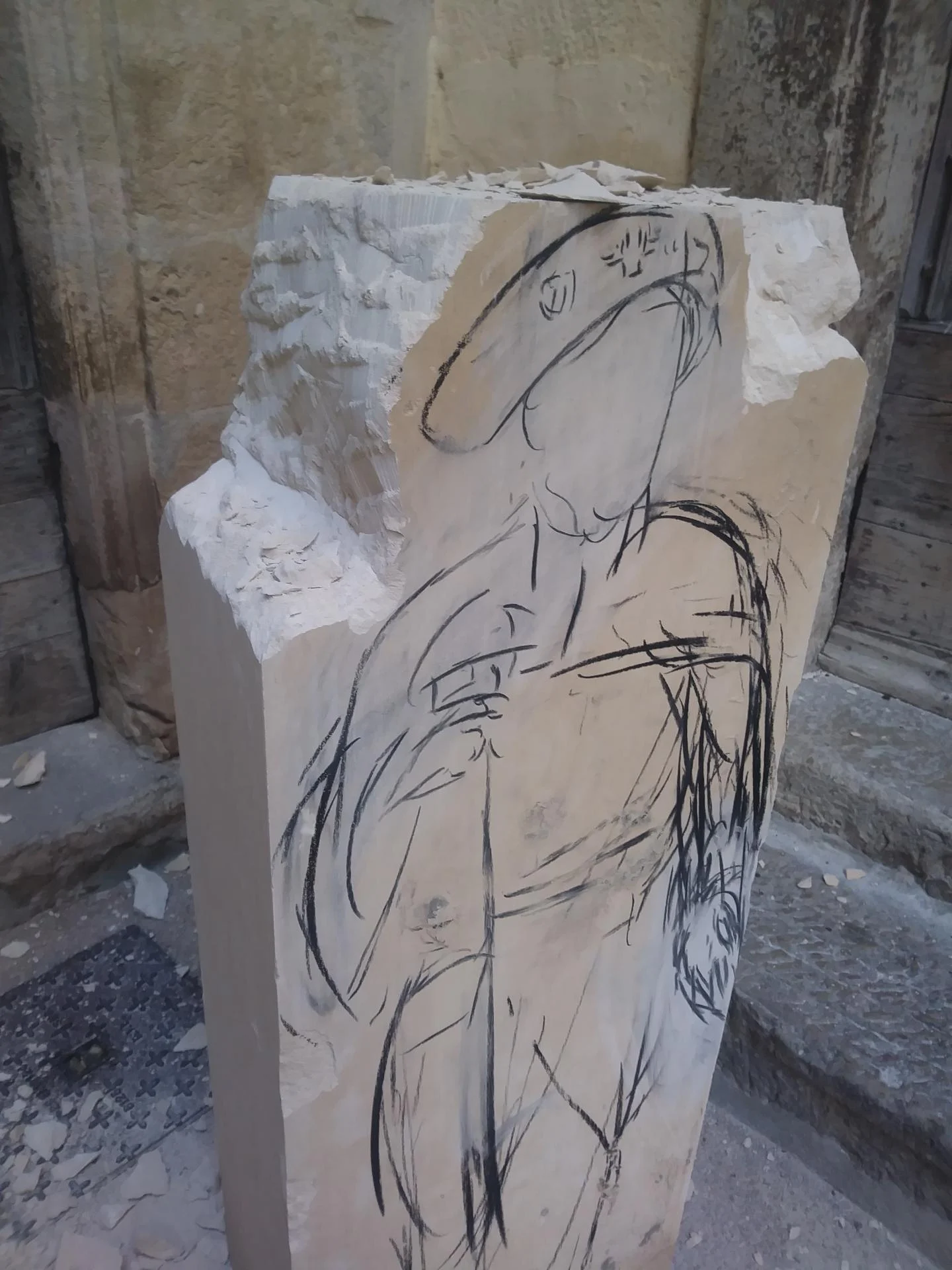Statue Saint Jacques de Compostelle en cours de création — bloc capable de pierre calcaire naturelle 130 cm avec dessin grandeur nature du pèlerin tracé au fusain sur la face, devant l'atelier du sculpteur Jean-Joseph Chevalier. Sculpture saint Jacques pierre calcaire sculptée main pour l'abbaye Saint-Paul de Wisques, étape jacquaire du nord de la France. Variante d'une œuvre originelle créée en 2003 pour la cathédrale de Lectoure