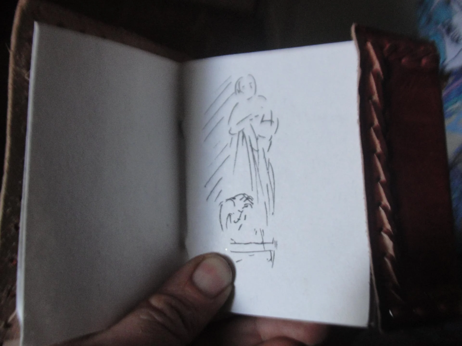 Le croquis préparatoire de la statue Saint Jean — un carnet de dessin tenu en main, esquisse au trait de la figure de l'évangéliste dans un rayon de lumière. La première pensée graphique avant la terre et la pierre. Art sacré — abbaye de Lagrasse 2016 — Jean-Joseph Chevalier.
