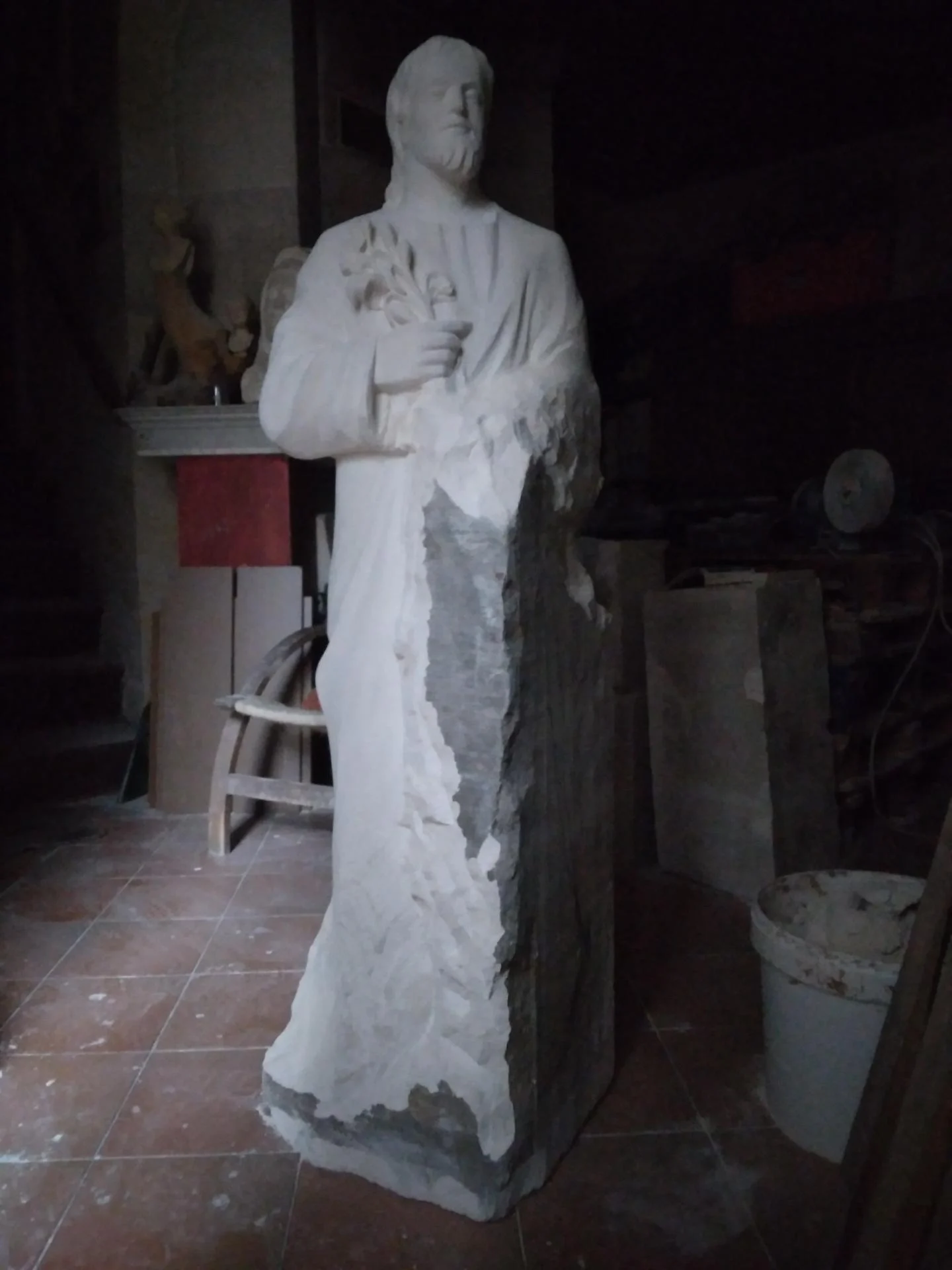 Vue d'atelier de la statue Saint Joseph Artisan en cours de taille directe sur pierre calcaire 120 cm, la silhouette complète du saint se révèle, drapé esquissé, deux mains apparentes, atelier de Brignoles, sculpteur d'art sacré Jean-Joseph Chevalier