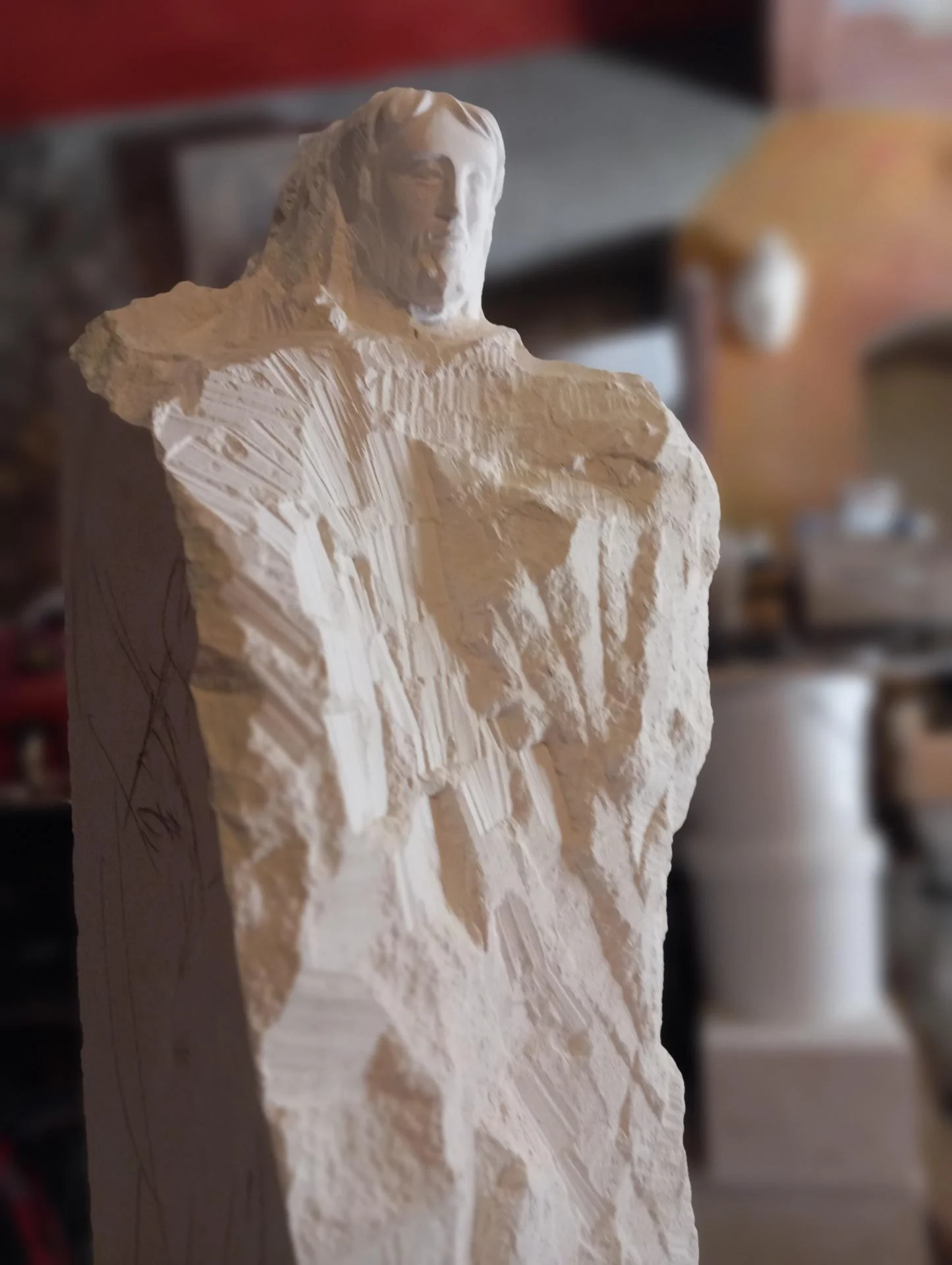 Vue d'atelier — la statue de saint Joseph en cours de taille directe, le visage et le buste dégagés tandis que le bas du drapé reste brut. La taille directe à la main est la technique traditionnelle du sculpteur sur pierre d'art sacré : sans moulage ni report mécanique, l'œuvre est arrachée au bloc de pierre calcaire naturelle geste après geste. Sculpteur d'art sacré chrétien Jean-Joseph Chevalier, atelier de Brignoles (Var, Provence), 2024.