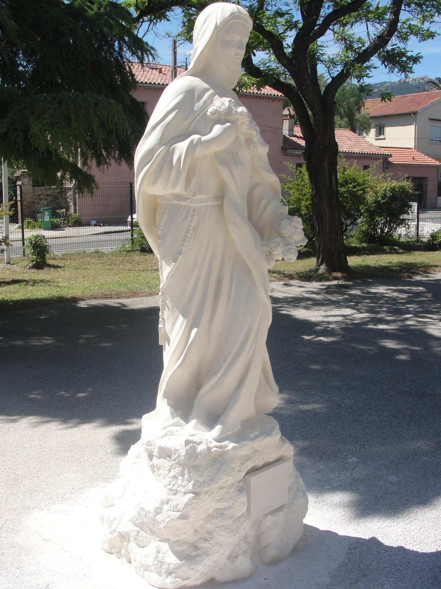 Détail iconographique de la statue Sainte Thérèse de Lisieux — main droite tenant ensemble les roses et le crucifix contre le cœur. Pierre véritable, pierre calcaire naturelle 160 cm, taille directe à la main par Jean-Joseph Chevalier, sculpteur d'art sacré chrétien en France. Geste intime unifiant l'union à la Croix de l'Époux et la promesse florale de la mission. Paroisse Sainte-Thérèse de Toulon, diocèse de Fréjus-Toulon, 2013.