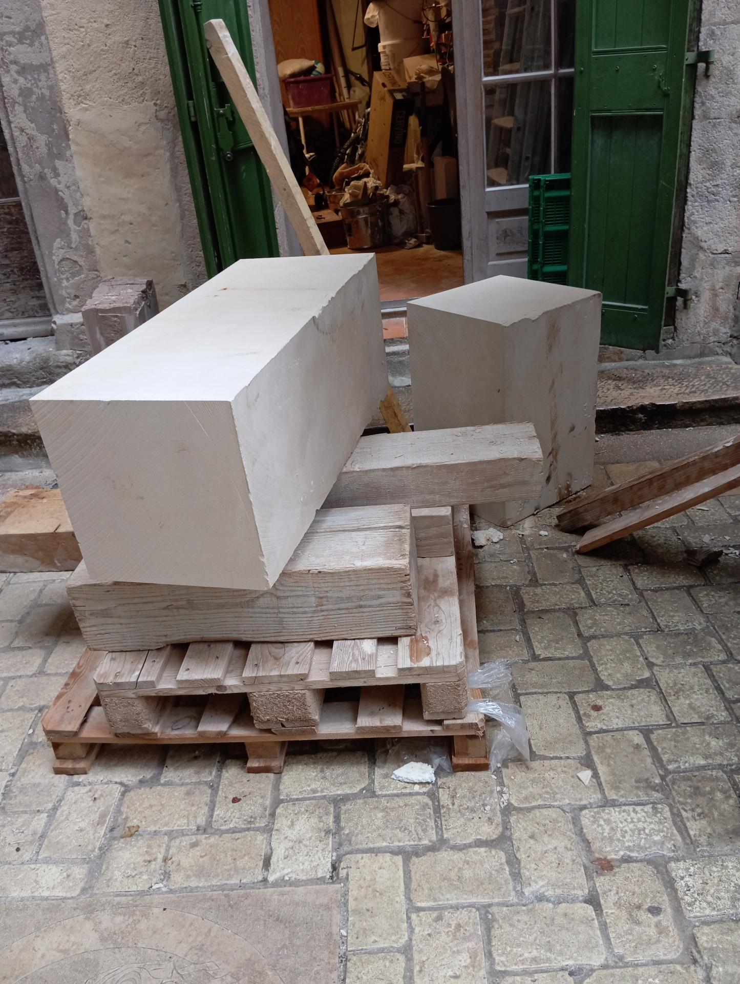 Vue d'atelier — le bloc de pierre calcaire naturelle brut, posé sur palette à l'entrée de l'atelier, avant la taille. Point de départ de la statue Saint Antoine le Grand : c'est de ce bloc compact que l'ermite va être arraché, geste après geste, en taille directe à la main, sans moulage ni report mécanique. Atelier Jean-Joseph Chevalier, sculpteur d'art sacré chrétien — Brignoles (Var, Provence), 2024.