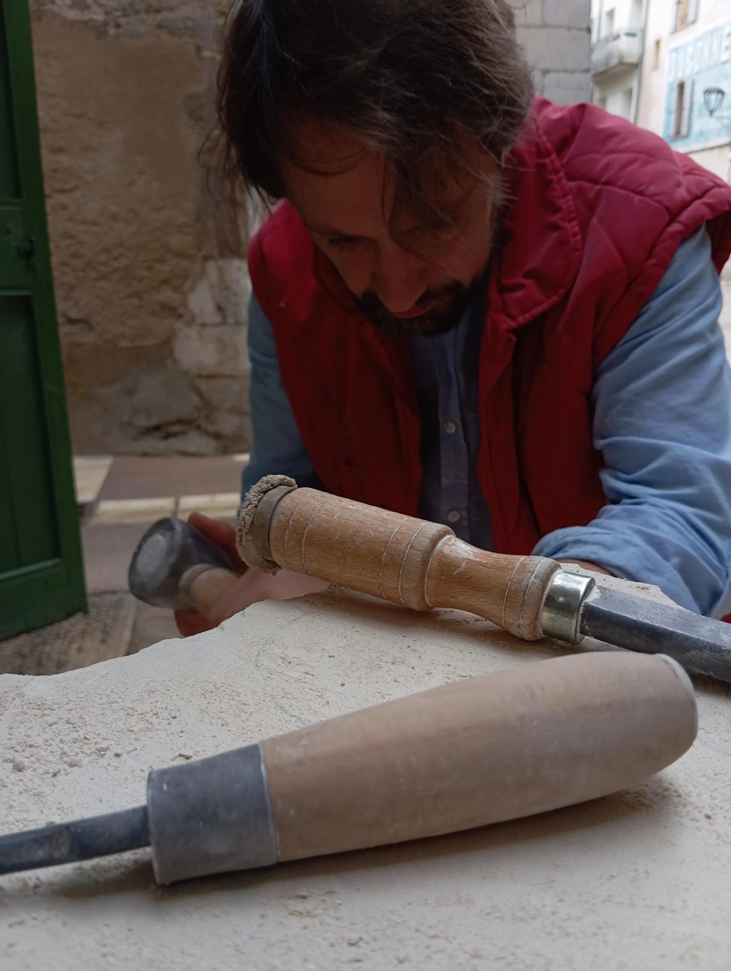Jean-Joseph Chevalier taille directement le bloc de pierre calcaire à la massette et au ciseau pour sculpter saint Antoine le Grand. Taille directe à la main, sans moulage ni report mécanique. Sculpteur d'art sacré chrétien, Brignoles (Var, Provence). Statue pour la basilique du Sacré-Cœur de Marseille.